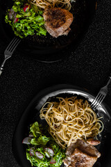 cooked chicken with spaghetti on black plates and on a black table
