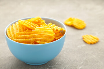 Potato chips in blue bowl on grey concrete background