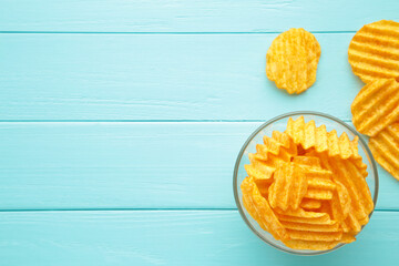 Golden potato chips in bowl on blue wooden background.