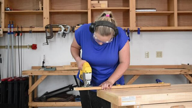 Female young adult woodworking cutting a plank with a hand electric saber saw.