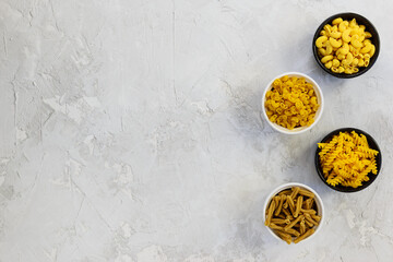 Different types of pasta from corn and buckwheat in bowls on a gray table. Healthy food, gluten free. Horizontal orientation, top view, copy space.