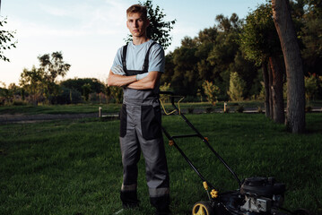 A young male gardener in overalls uses a lawn mower.