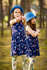 two little girls in blue hats are posing in the spring pine forest