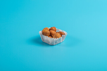 A serving of hazelnuts in a paper muffin cup on a blue background.