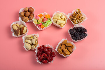 Fototapeta na wymiar A serving of assorted candied fruit, dried cherries, almonds, raisins, walnuts and hazelnuts in paper muffin cups on a pink background. Copyspace.