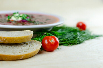 An appetizing portion of beetroot soup with sour cream on a wooden table. Russian kitchen. Borsh. Dill and spring onions.