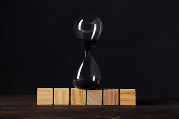 Hourglass or sandglass on cube wooden blocks, place for text, on wooden table with dark background.