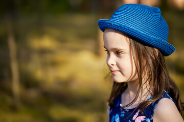 little girl in a blue hat posing in the spring pine forest