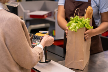 Hand of mature female customer with plastic card over payment machine