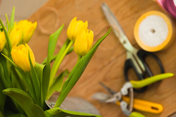 Yellow tulips in a bucket before selling in a flower shop are standing on an Arab table with scissors and secateurs.