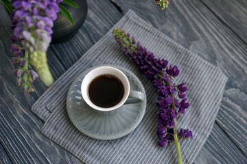 Small mug with black coffee and lupins on a wooden table