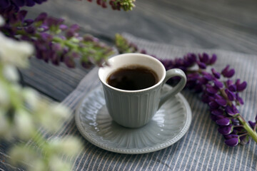 Small mug with black coffee and lupins on a wooden table