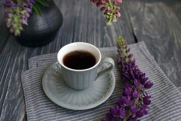 Small mug with black coffee and lupins on a wooden table