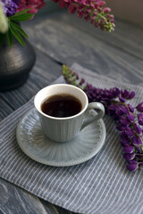 Small mug with black coffee and lupins on a wooden table