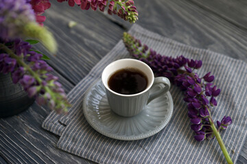 Small mug with black coffee and lupins on a wooden table