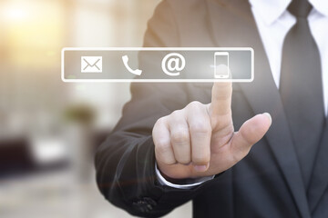 Businessman hand pressing a contact us icons on blur office lights background.