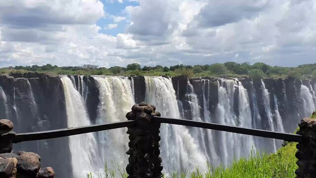 Walking along the Stunning Victoria Falls, the largest Waterfall with a dramatic blue Sky, Zambia, and spray, steam in the Air