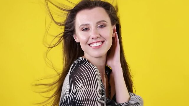 Beautiful young brunette girl with fluttering hair with wind on yellow background