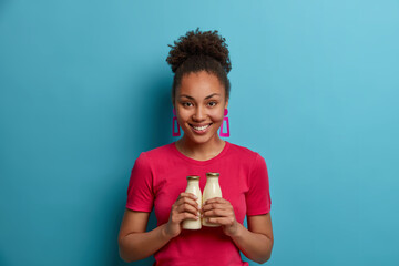 Pleased woman vegan holds bottles of fresh organic coconut milk, has healthy eating, smiles...