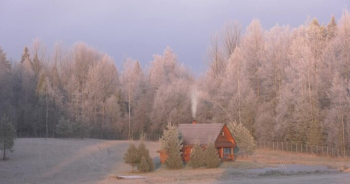 A house on the edge of the forest next to the freeze pond. Surrounded by frosted trees in complete silence of the estate, smoke blows from the chimney.