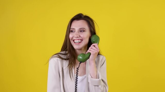 Happy woman talking on green dial phone on yellow background. Retro, vintage concept