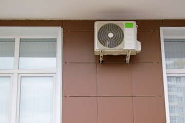 Air conditioning attached to the ventilated facade of the building. Brown wall made of tiled...