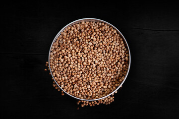 Colored coriander spices in a bowl, top view on a dark background, seasoning for delicious cooking