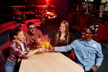 Four multi-ethnic friends in casualwear clinking with glasses of orange juice