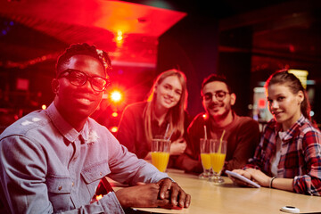 Happy guy of African ethnicity sitting by table with his intercultural friends