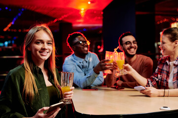 Pretty blond girl with glass of orange juice and mobile phone sitting by table