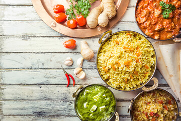 Different bowls with assorted indian food on white wooden background, top view. Dishes and appetizers of indian cuisine. Chicken, curry rice, lentils, paneer, chapati and spices.