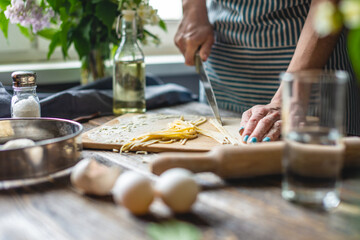 Woman is cutting raw dough with a knife to make homemade noodles. Concept of process of cooking handmade pasta