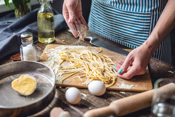 Woman is carefully sprinkling flour on fresh homemade noodles. Concept of cooking handmade pasta in...