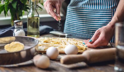 Woman is carefully sprinkling flour on fresh homemade noodles. Concept of cooking handmade pasta in a cozy atmosphere