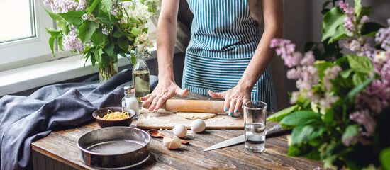 The woman is rolling out fresh dough for making pasta in a cozy atmosphere. Concept of cooking delicious food at home