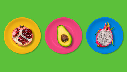 Avocado, red pomegranate and pitaya in colorful plates on a green background. The concept of vegetarian food. Fashionable creative and summer style. Minimal design Art.