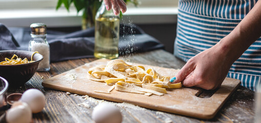 Woman is carefully sprinkling flour on fresh homemade noodles. Concept of cooking handmade pasta in a cozy atmosphere
