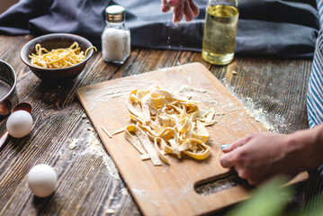 Woman is carefully sprinkling flour on fresh homemade noodles. Concept of cooking handmade pasta in...