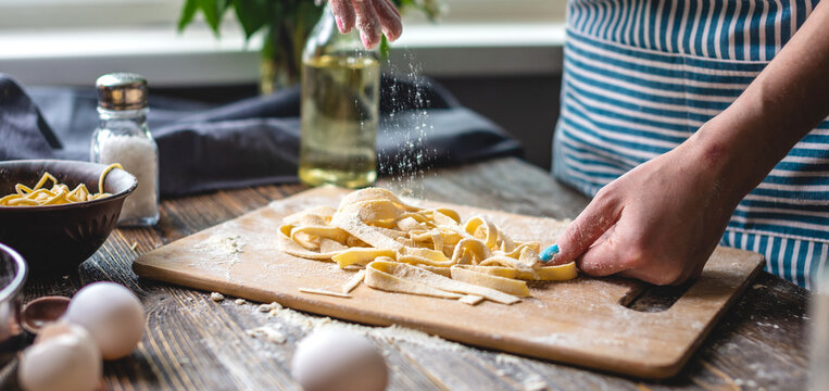 Woman is carefully sprinkling flour on fresh homemade noodles. Concept of cooking handmade pasta in a cozy atmosphere