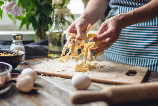 Woman is carefully holding raw homemade noodles in her hands. Process of cooking handmade pasta in a cozy atmosphere