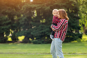 Fototapeta premium Happy young mother is playing with her baby in a park on a green lawn.Concept of a happy family. Mothers Day. Mother and son have activities together on holidays.