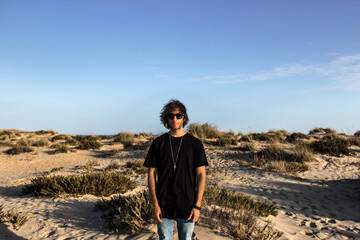 Modelo masculino con gafas de sol y camiseta negra en la playa