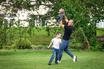 Happy young daddy is playing with  her baby in a park on a green lawn.Concept of a happy family. Fathers Day. Dad and son have activities together on holidays.