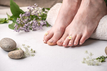 Obraz na płótnie Canvas Cared beautiful women's feet with beige nail polish on a white background with flowers, stones and a towel. Concept of a relaxing Spa pedicure