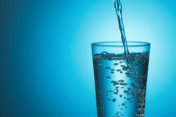 Fresh water pours into a glass on a blue background.