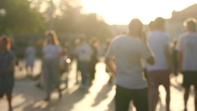 Video footage of many blurry people of different ages walking in streets of sunny summer sunset city.