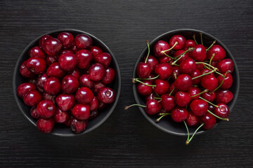 Two varieties of cherries lies in dark plates on a dark background