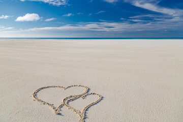 Two hearts drawn on a sandy beach with sea horizon. Exotic couple travel and summer holiday concept. Tropical love landscape