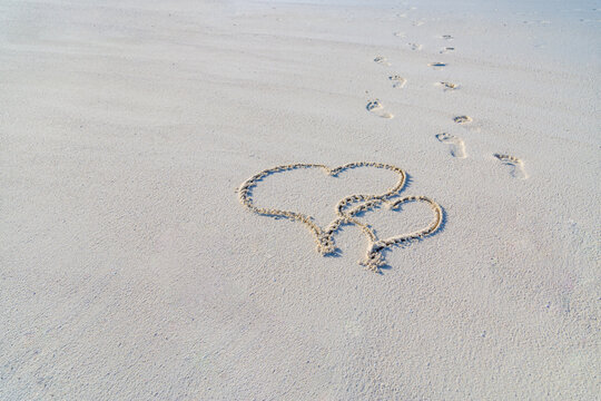 Two hearts drawn in white sand, love concept. Honeymoon or anniversary travel concept. Summer holiday vacation for couples