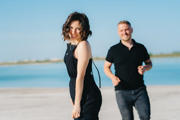 young couple a guy with a girl in black clothes are walking on the white sand